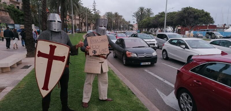 Dos membres del grup amb escut i pancarta al passeig Sagrera de Palma, entre palmeres i trànsit.