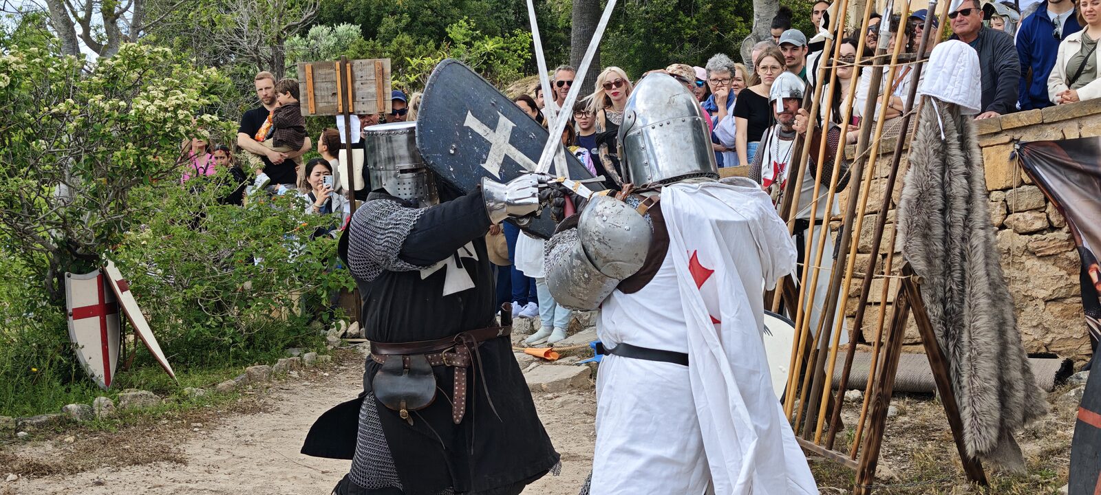 Dos combatents amb elms tancats i escuts creuen espases davant el públic.